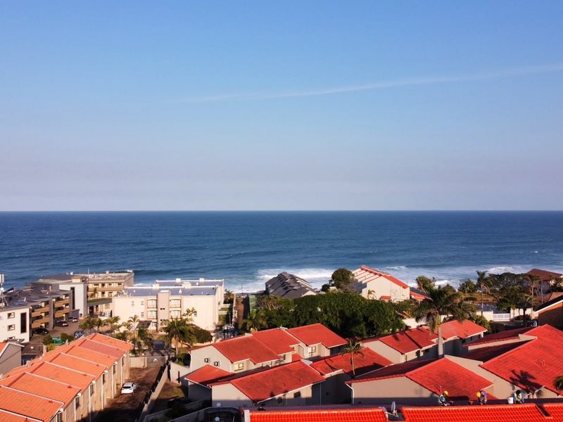 An elevated aerial view showcasing the coastal residential complex with red-tiled roofs overlooking the ocean.