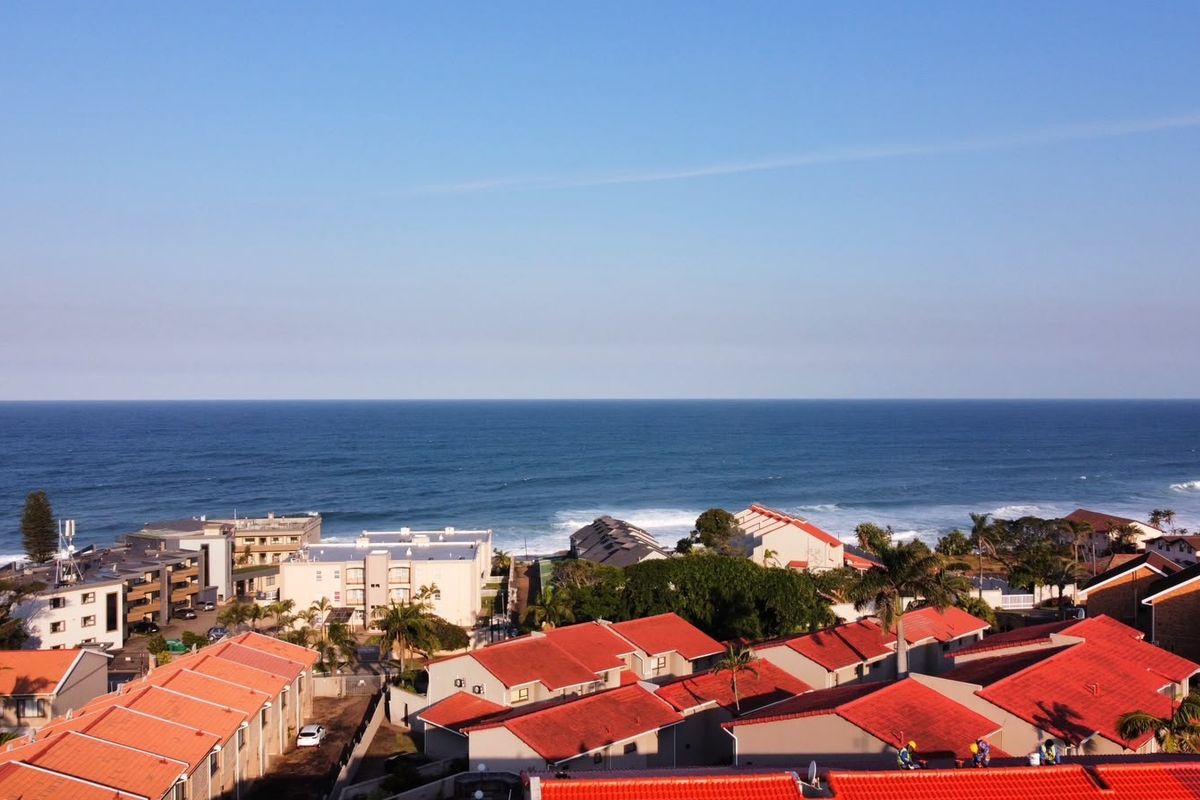 An elevated aerial view showcasing the coastal residential complex with red-tiled roofs overlooking the ocean.