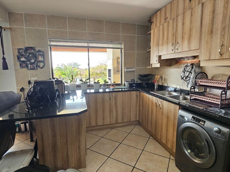 Functional kitchen featuring wood-look laminate cabinetry, granite countertops, tiled backsplash, and integrated laundry plumbing, with a window overlooking the outdoor area.