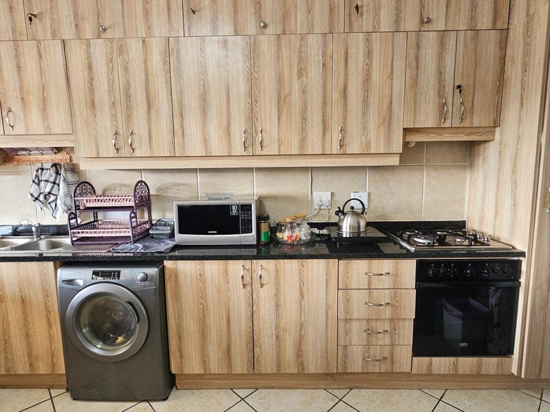 A functional kitchen featuring wood-look laminate cabinetry, granite countertops, a built-in oven, gas hob, and integrated space for a washing machine.