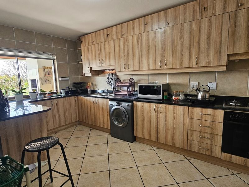 A functional kitchen featuring wood-look laminate cabinetry, granite countertops, built-in oven, gas hob, and integrated laundry appliance with tiled flooring.
