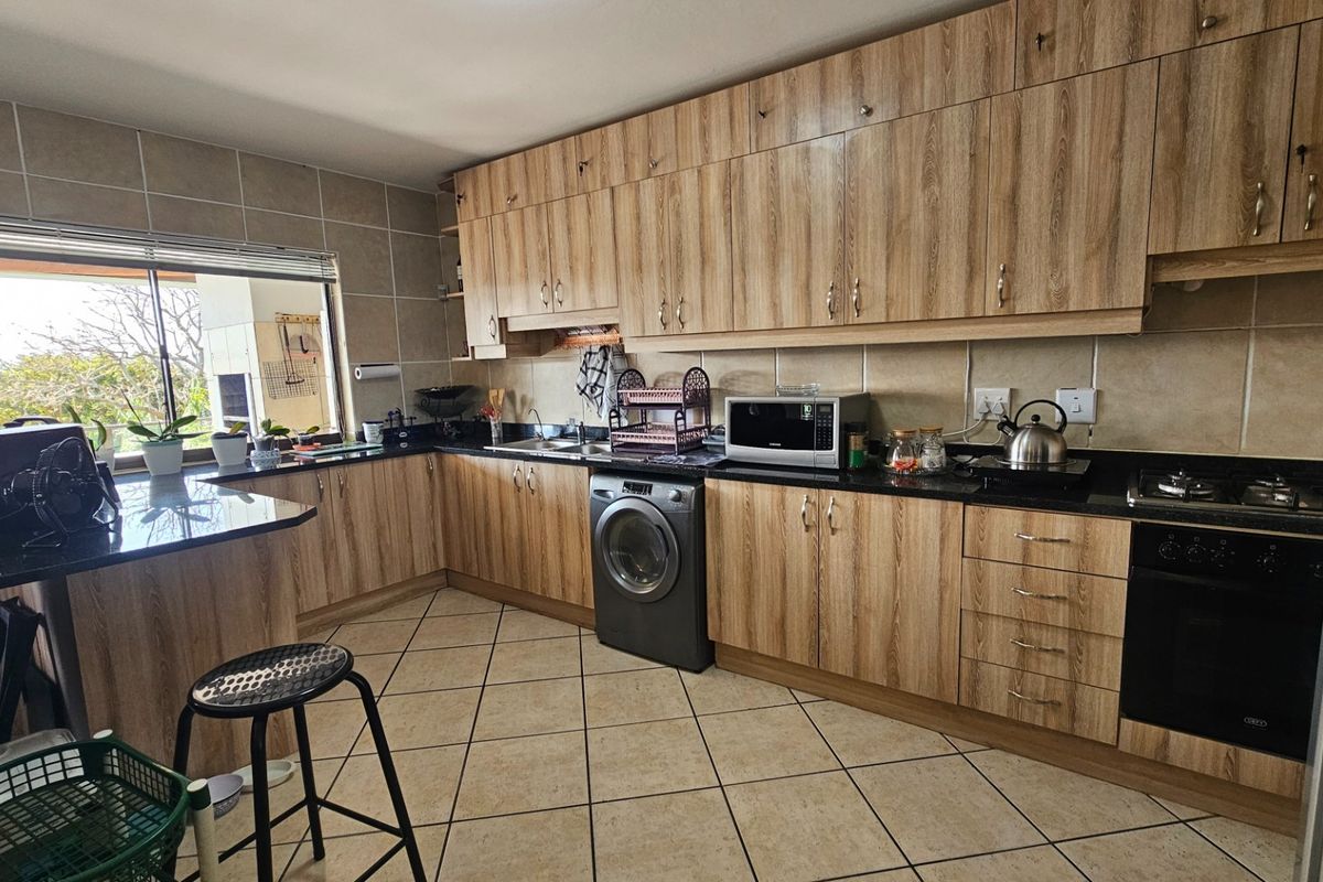 A functional kitchen featuring wood-look laminate cabinetry, granite countertops, built-in oven, gas hob, and integrated laundry appliance with tiled flooring.
