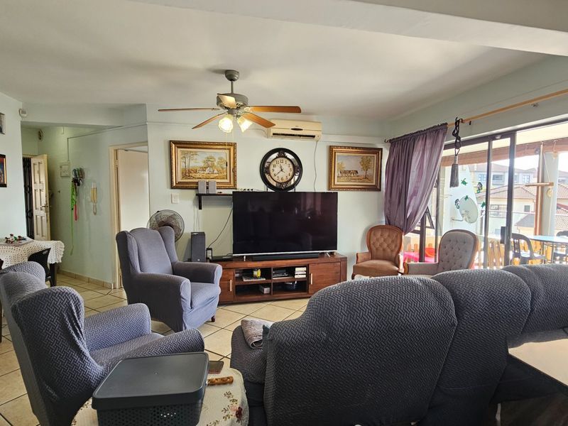 A comfortable living room featuring tiled flooring, a ceiling fan, wall-mounted air conditioning, and direct access to a balcony through sliding glass doors.