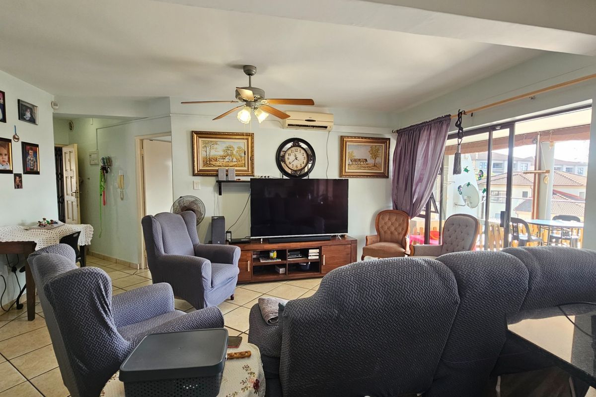 A comfortable living room featuring tiled flooring, a ceiling fan, wall-mounted air conditioning, and direct access to a balcony through sliding glass doors.