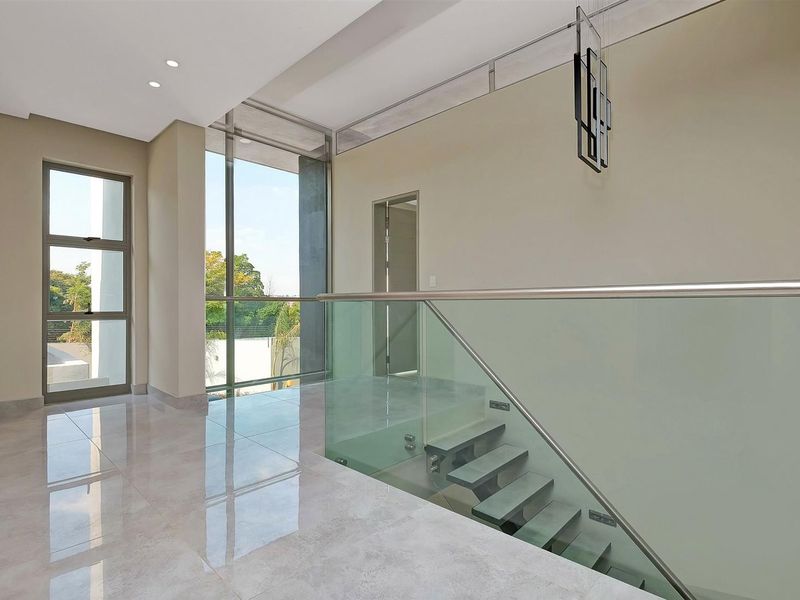 A bright and modern landing area featuring a sleek floating staircase with a glass balustrade, large format floor tiles, and expansive windows.