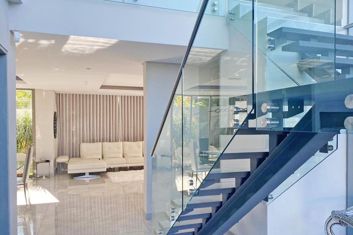 Modern open-plan living area featuring a contemporary staircase with a glass balustrade, polished tiled flooring, and recessed ceiling lighting.
