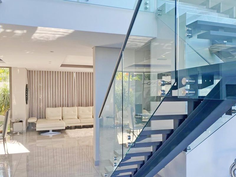 Modern open-plan living area featuring a contemporary staircase with a glass balustrade, polished tiled flooring, and recessed ceiling lighting.