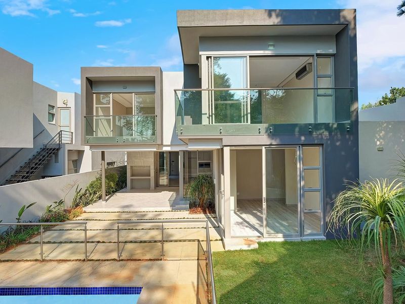 Modern double-story rear elevation featuring a swimming pool, covered patio with built-in braai, and upper-level balconies with glass balustrades.