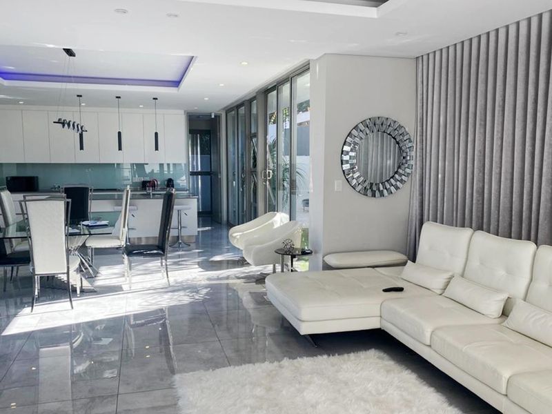 Modern open-plan living and dining area featuring high-gloss tiled floors, recessed ceiling lighting, and seamless flow to the outdoor patio through large sliding glass doors.