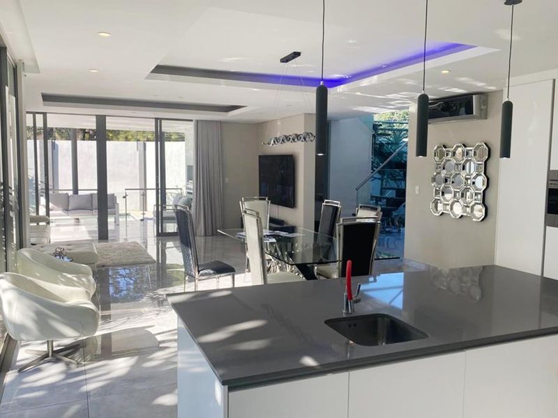 Modern open-plan living area featuring a sleek kitchen island, high-end finishes, recessed lighting, and seamless flow to the outdoor patio through large sliding glass doors.