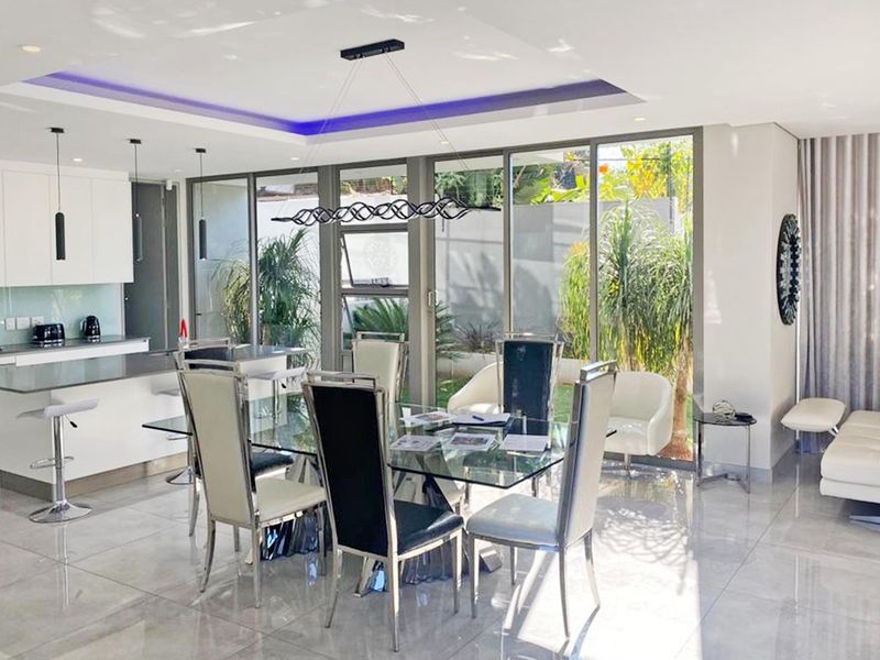Modern open-plan living and dining area featuring a sleek kitchen island, high-gloss tiled floors, and expansive glass doors opening to the garden.