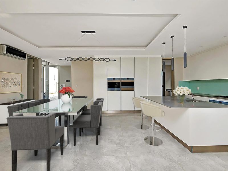 Modern open-plan kitchen and dining area featuring a large island, built-in double ovens, sleek cabinetry, and contemporary pendant lighting.