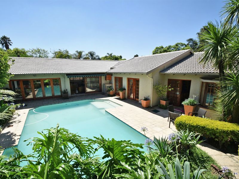 A well-maintained outdoor pool area featuring a paved patio, swimming pool, and direct access to the home through multiple wooden-framed glass doors.