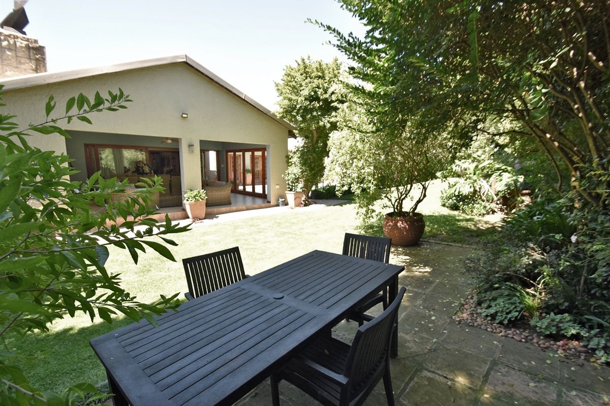 Rear view of the property featuring a covered patio, paved outdoor dining area, and a well-maintained garden with mature trees.