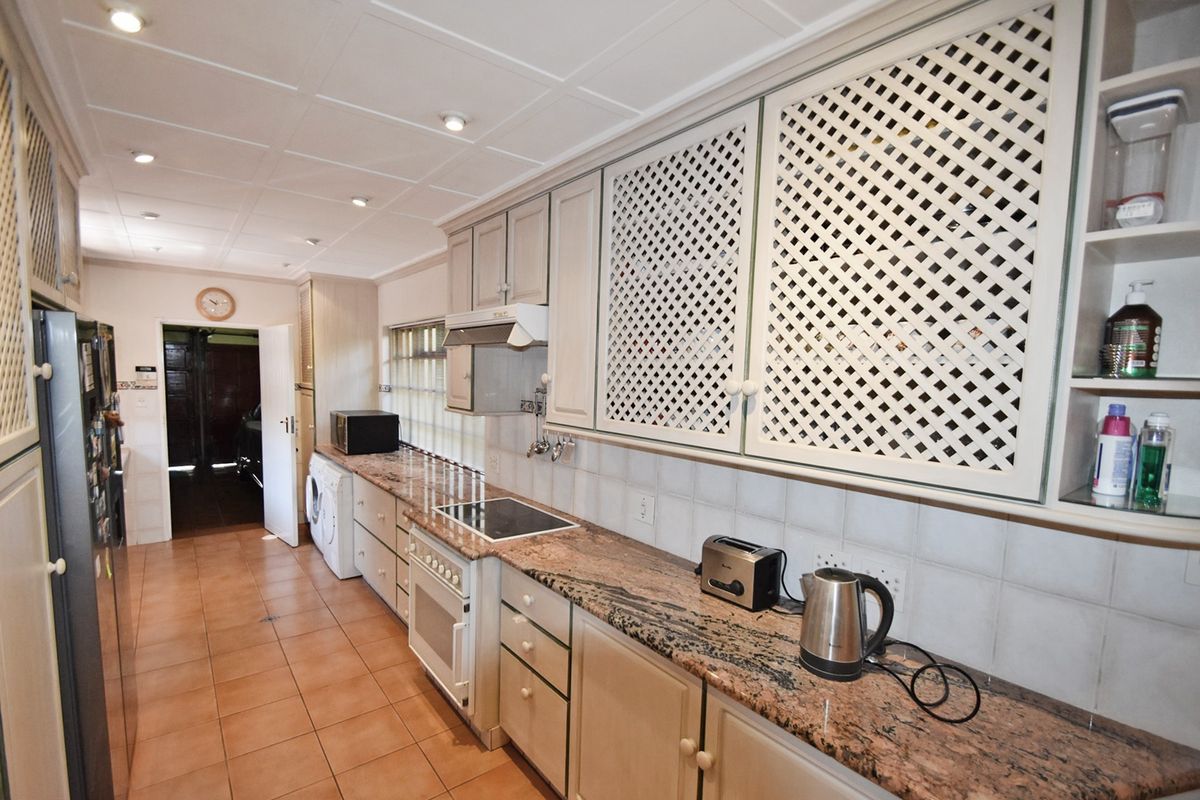 A functional kitchen featuring granite countertops, tiled flooring, built-in oven with hob, and distinctive lattice-style cabinetry with ample storage space.