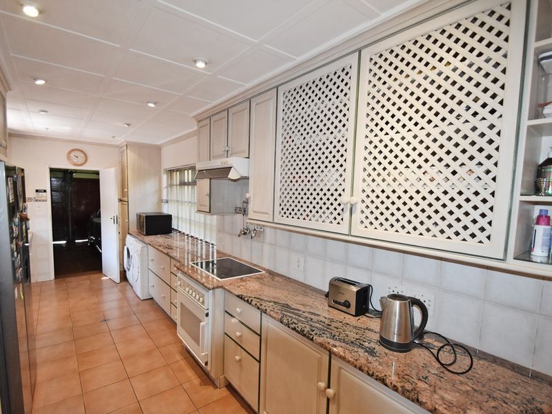 A functional kitchen featuring granite countertops, tiled flooring, built-in oven with hob, and distinctive lattice-style cabinetry with ample storage space.