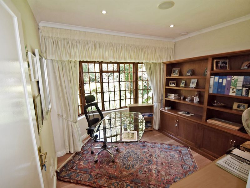 A home office featuring built-in wooden cabinetry, laminate flooring, and a large bay window that provides natural light.