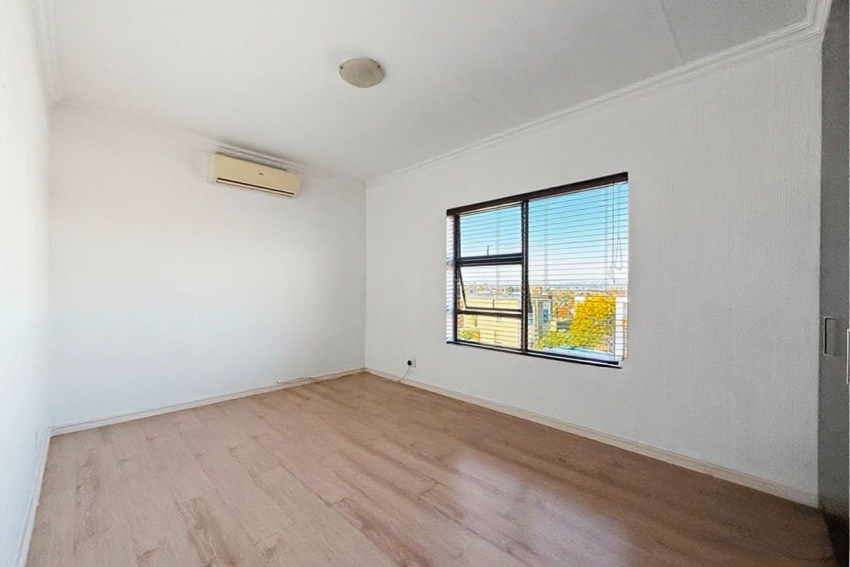 A bright, empty bedroom featuring laminate flooring, a built-in cupboard, and an air conditioning unit, offering a clean canvas for personalization.