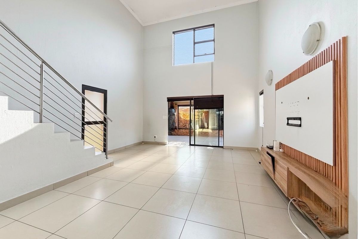 Spacious open-plan living area featuring high ceilings, tiled flooring, a modern staircase with stainless steel balustrade, and a built-in media unit.