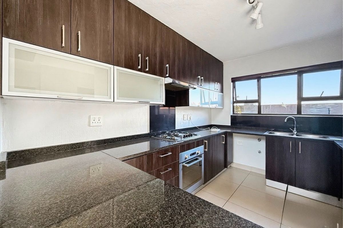 Modern kitchen featuring dark wood cabinetry, granite countertops, built-in oven, gas hob, and tiled flooring with ample natural light.