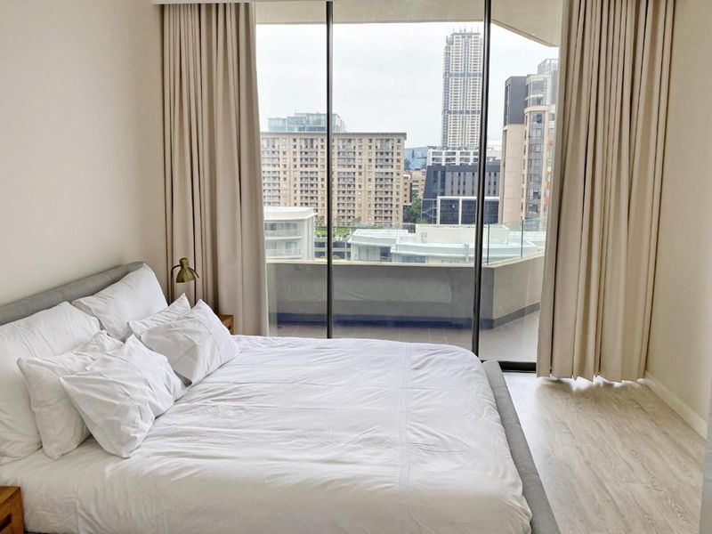A bright bedroom featuring floor-to-ceiling windows with access to a private balcony and expansive city views.