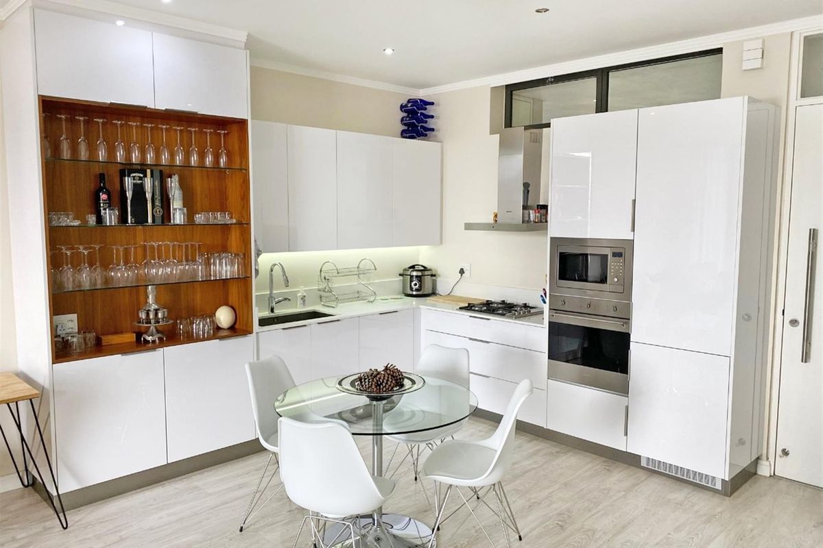 Modern kitchen featuring high-gloss white cabinetry, integrated stainless steel appliances, gas hob, and elegant wooden display shelving with recessed lighting.