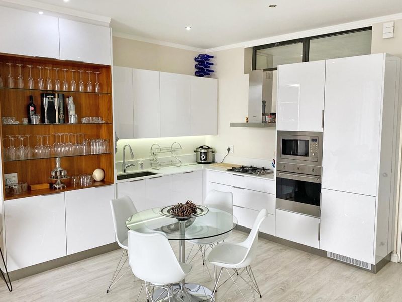 Modern kitchen featuring high-gloss white cabinetry, integrated stainless steel appliances, gas hob, and elegant wooden display shelving with recessed lighting.