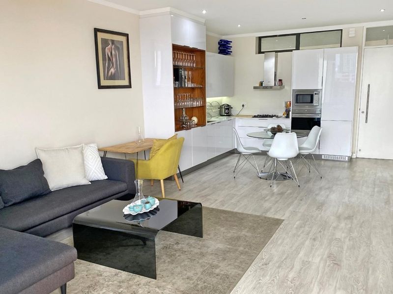 Modern open-plan living area featuring a sleek kitchen with integrated appliances, high-gloss cabinetry, and light wood-look laminate flooring throughout.