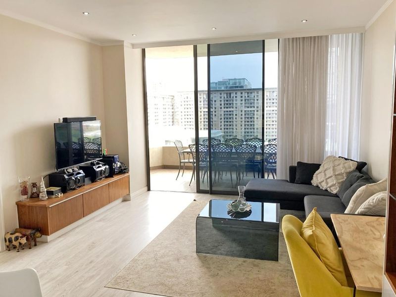 Bright and modern living room featuring laminate flooring, recessed downlights, and large sliding glass doors leading to an outdoor balcony area.