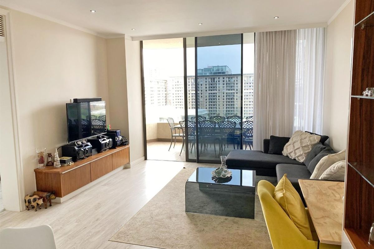 Bright and modern living room featuring laminate flooring, recessed downlights, and large sliding glass doors leading to an outdoor balcony area.