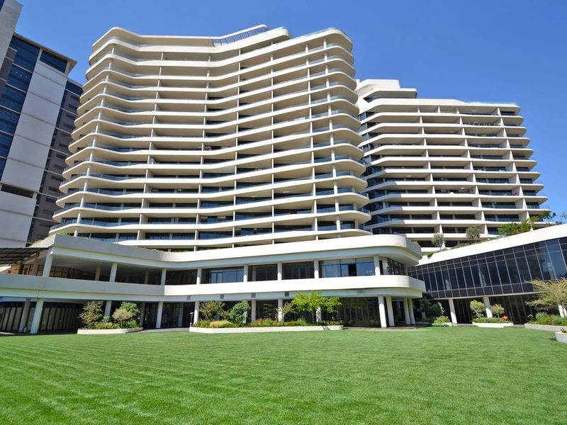 A view of the rear elevation of a modern high-rise apartment building featuring tiered balconies and a well-maintained landscaped lawn area.