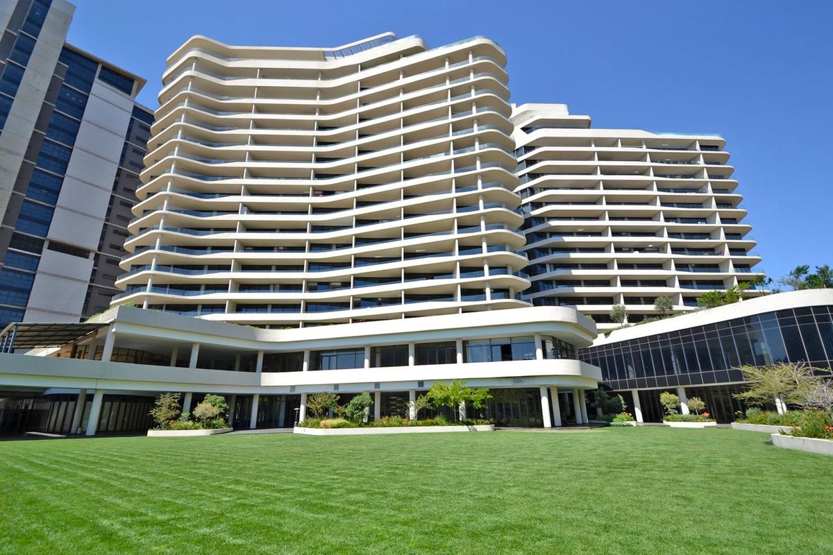 A view of the rear elevation of a modern high-rise apartment building featuring tiered balconies and a well-maintained landscaped lawn area.