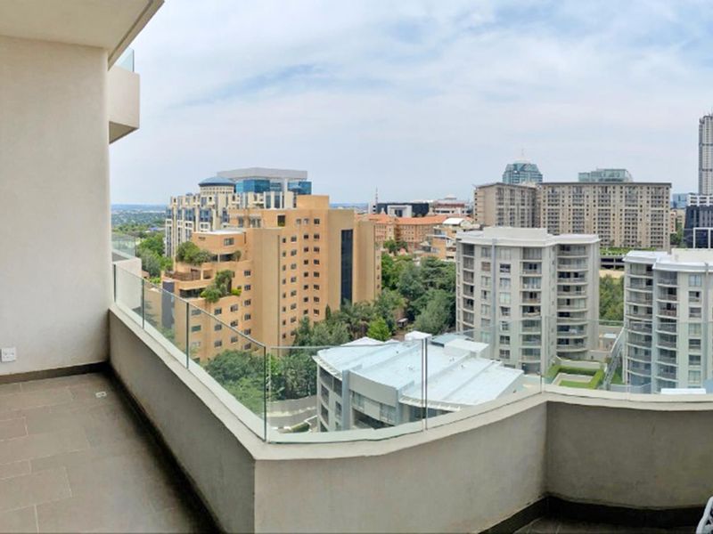 A spacious apartment balcony featuring a modern glass balustrade and tiled flooring, offering expansive views of the surrounding city skyline.