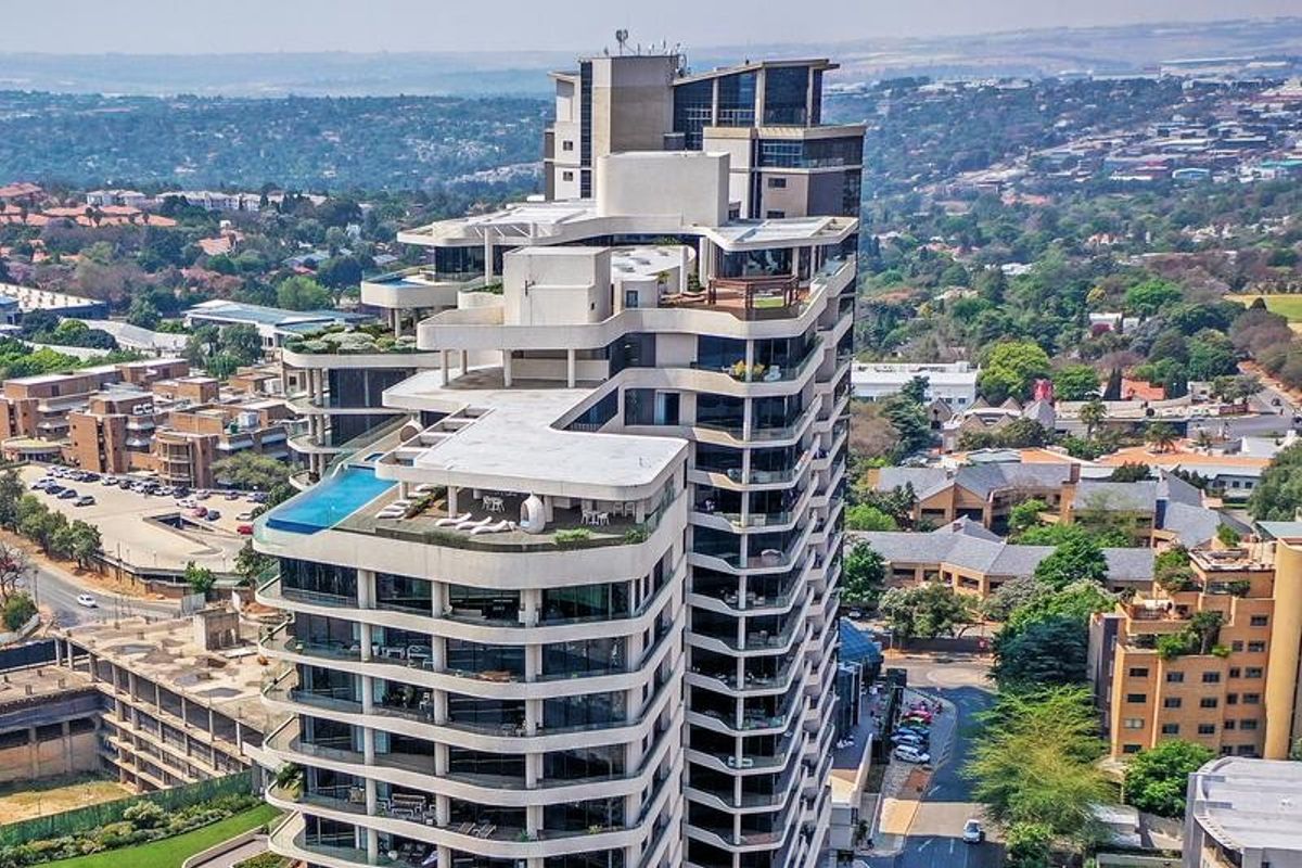 Aerial view of a modern high-rise apartment building featuring extensive balconies, a rooftop swimming pool, and landscaped terrace areas.