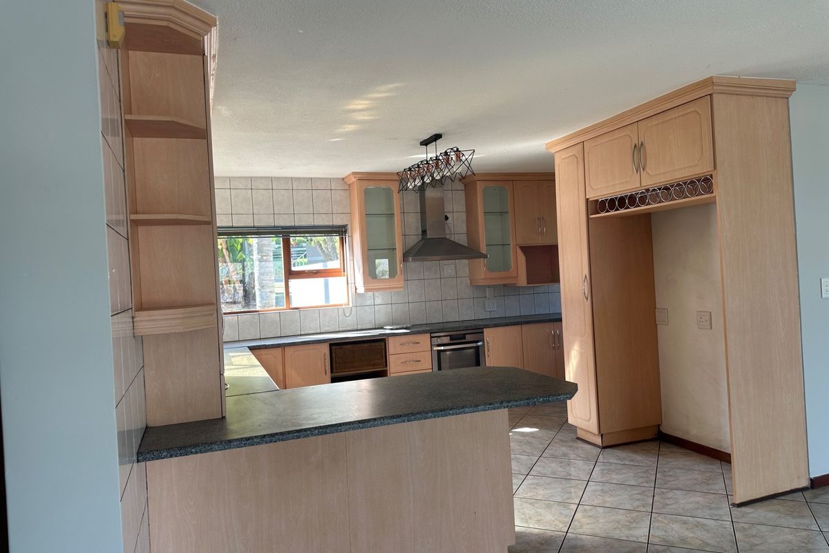 A functional kitchen featuring light wood cabinetry, laminate countertops, a built-in oven, and a breakfast bar, finished with tiled flooring and backsplash.