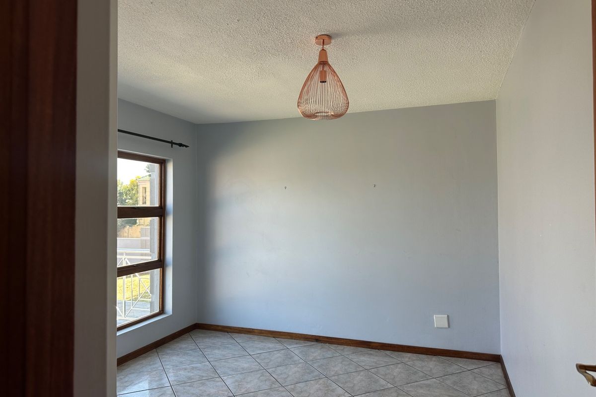 A bright, empty bedroom featuring tiled flooring, a textured ceiling, and a large window, providing a clean canvas for personalization.