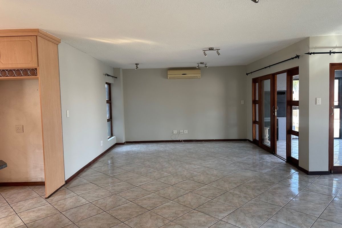 Spacious, empty living area featuring tiled flooring, a wall-mounted air conditioning unit, and large wooden-framed glass doors leading to an outdoor space.
