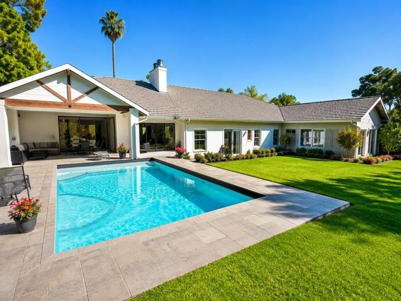 A well-maintained rear exterior featuring a sparkling swimming pool, a spacious covered patio area, and a manicured lawn.