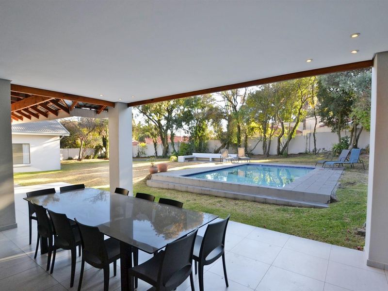A spacious covered patio overlooking a private garden and swimming pool, featuring tiled flooring and recessed lighting, ideal for outdoor entertaining.