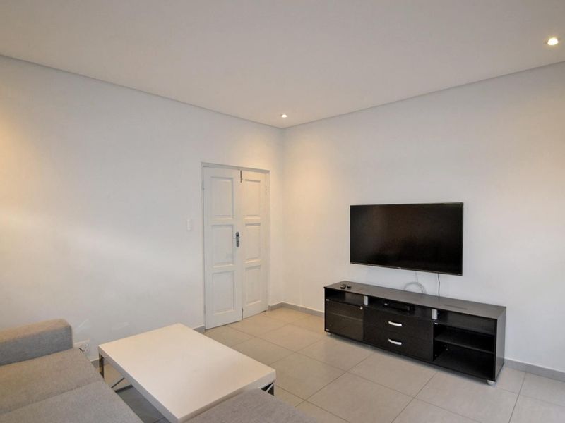 A clean and minimalist living room featuring neutral tiled flooring, recessed downlighting, and a double door entrance.