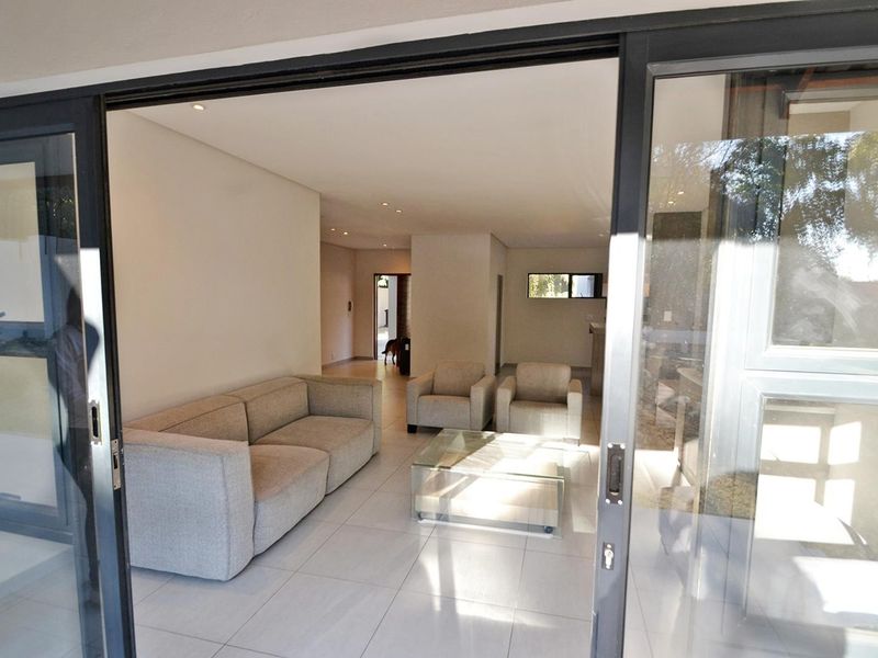 Bright open-plan living area featuring large sliding glass doors, neutral tiled flooring, and modern recessed downlighting.