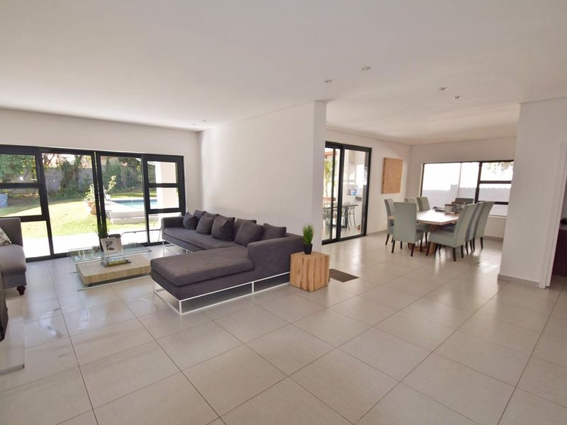 Spacious open-plan living and dining area featuring large format floor tiles, recessed lighting, and expansive sliding glass doors providing seamless access to the garden.