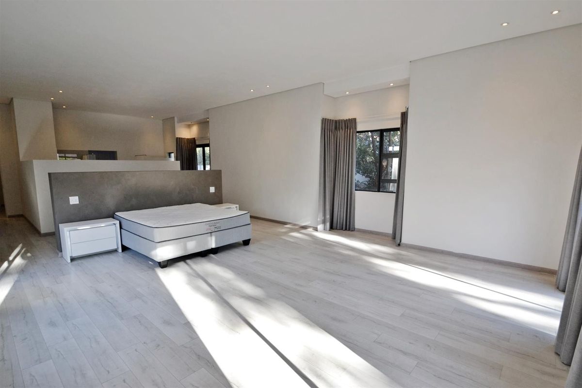 Spacious bedroom featuring modern laminate flooring, recessed downlighting, and a central partition wall creating a distinct sleeping area.