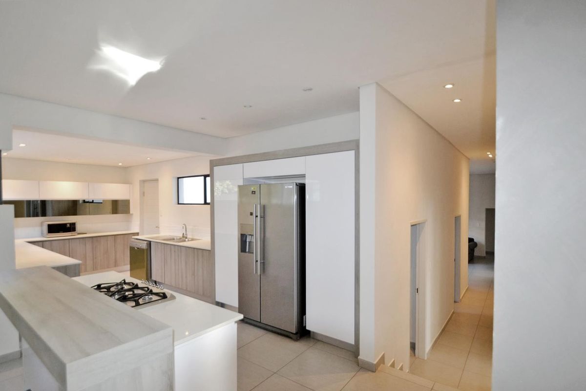 Modern open-plan kitchen featuring sleek cabinetry, stone countertops, a gas hob, and integrated appliances, seamlessly flowing into the adjacent hallway.