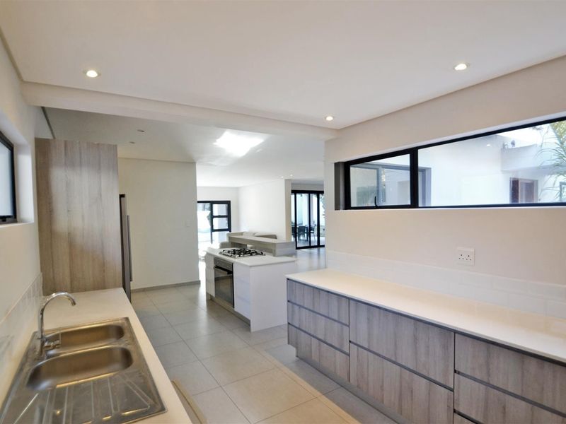 Modern open-plan kitchen featuring sleek cabinetry, a central island with gas hob, and integrated oven, flowing seamlessly into the adjacent living area.