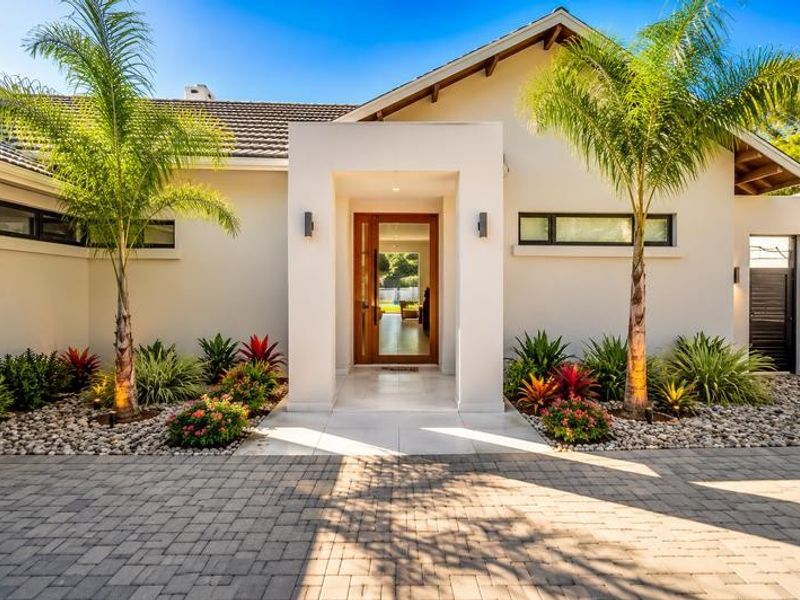 Modern front facade featuring a paved driveway, landscaped garden beds, and a prominent timber entrance door with tiled porch area.