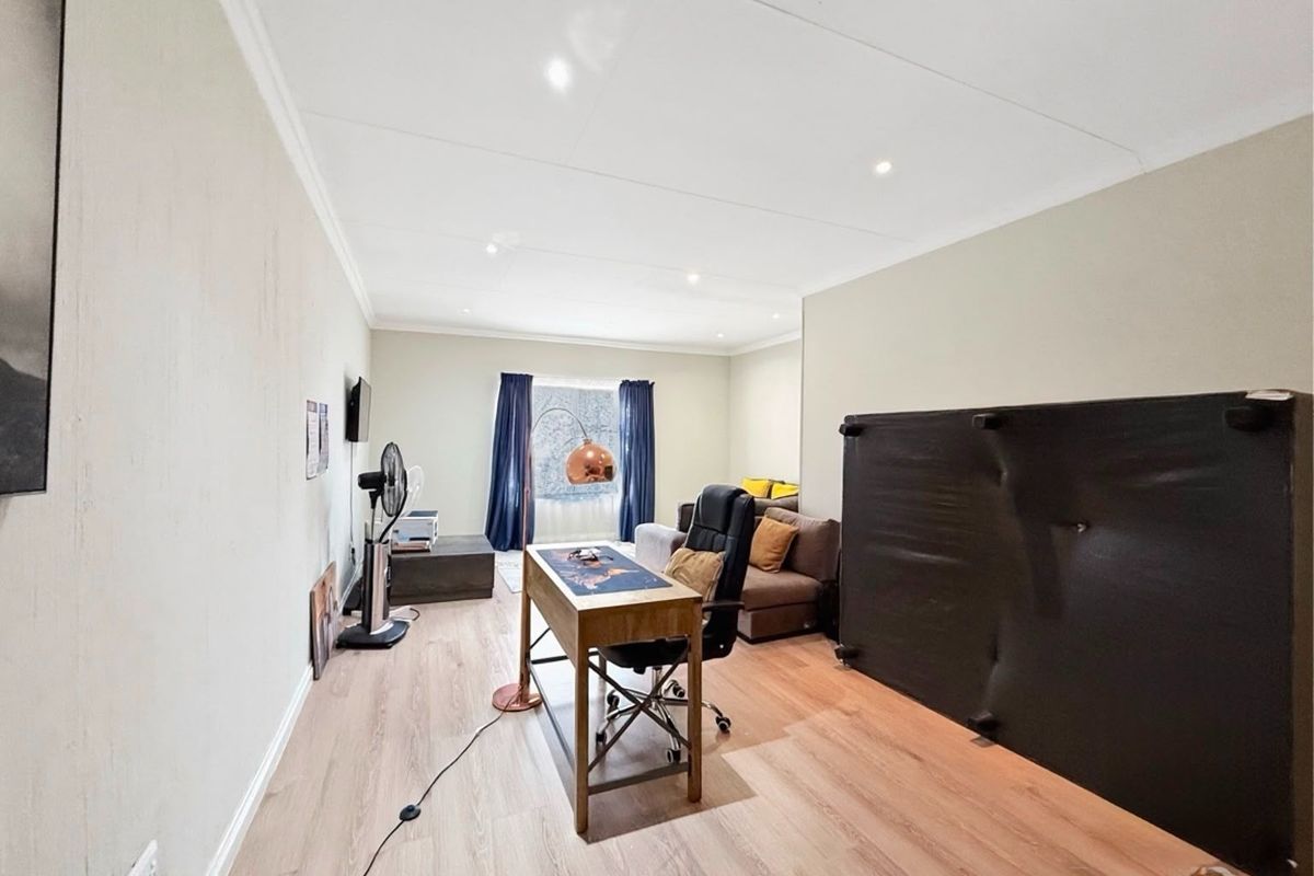 A spacious living area featuring light-toned laminate flooring, recessed downlighting, and coved cornicing, offering a versatile layout for various furniture arrangements.