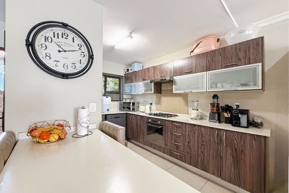A functional kitchen featuring wood-grain cabinetry, stone countertops, a gas hob, built-in oven, and integrated dishwasher, complemented by tiled flooring.