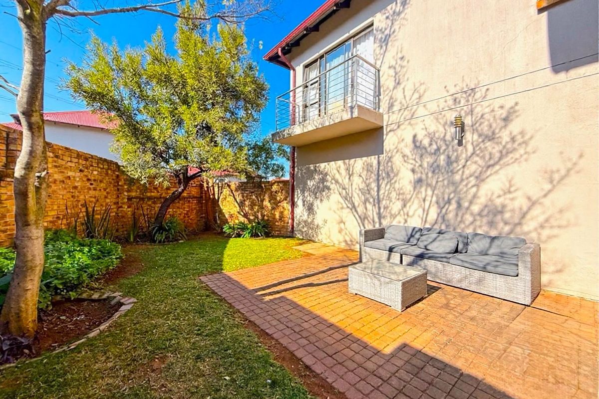 A private rear garden featuring a paved patio area, established landscaping, and an upper-level balcony with a metal balustrade.