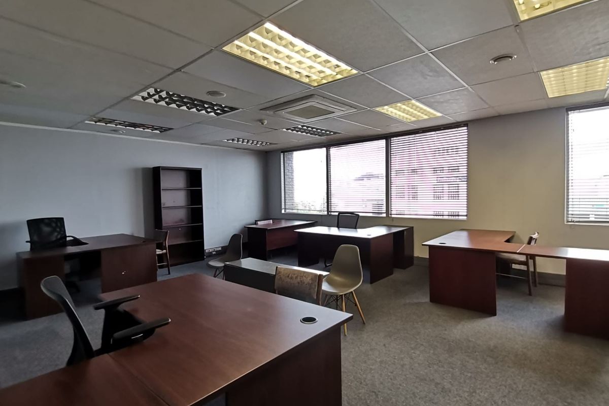 Spacious open-plan office area featuring suspended ceilings, recessed lighting, and large windows with venetian blinds, providing a functional workspace environment.